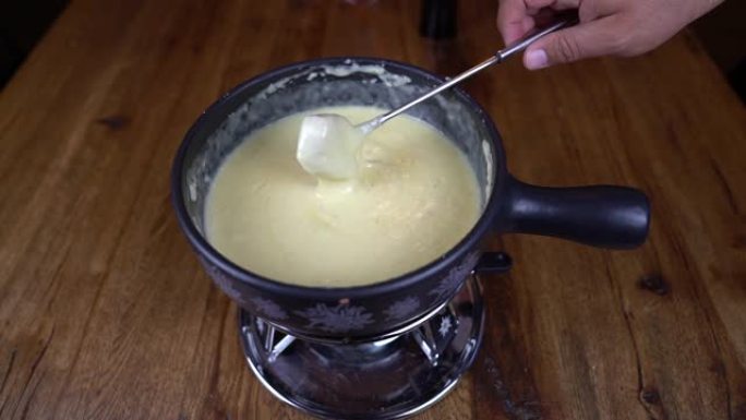 吃瑞士奶酪火锅。融化的奶酪放在锅里，用叉子蘸一块面包