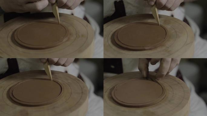 粘土大师用木刀切掉一个均匀的粘土圈，用宜兴粘土为茶壶做盖子。手工制作的陶制茶壶宜兴茶道。紫色陶茶壶。