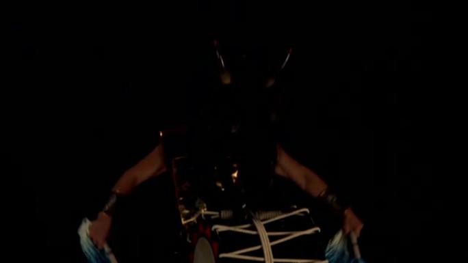 艺术家鼓手Taiko戴着假发，戴着角和化妆鼓，在黑暗的背景下在舞台上。日本神话中的恶魔。