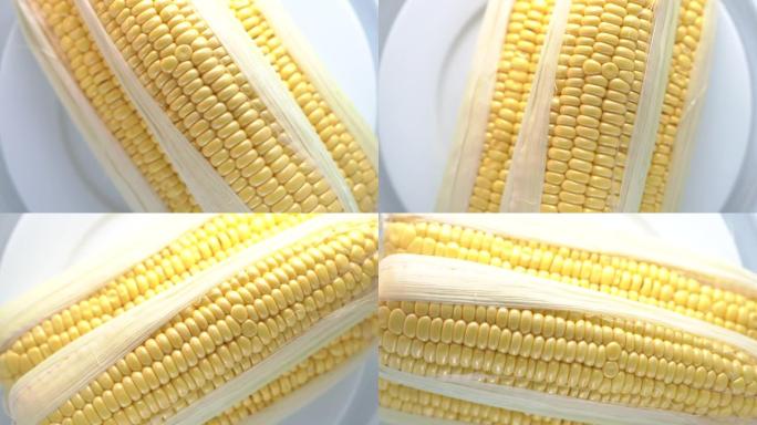 新鲜生甜玉米棒在白盘旋转特写俯视图。