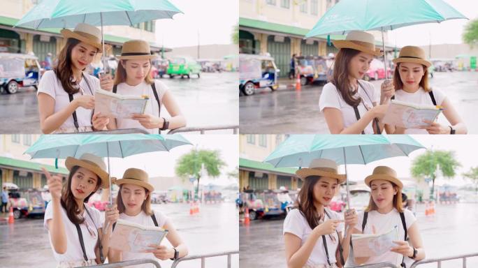 妇女和朋友在看地图。亚洲妇女享受曼谷Wat Pho在曼谷市的地标。两名亚洲妇女在雨天撑伞探索泰国主要