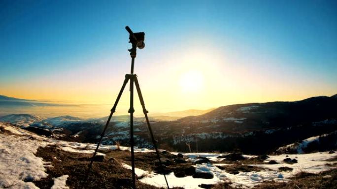 在日出背景中隔离的三脚架上的相机。日出时，三脚架上的相机剪影与山背景