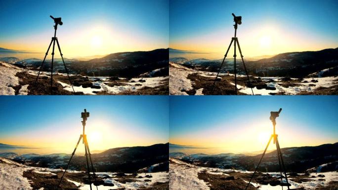 在日出背景中隔离的三脚架上的相机。日出时，三脚架上的相机剪影与山背景
