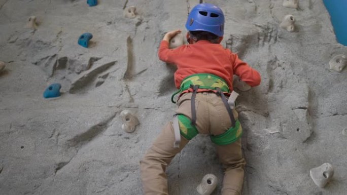 男孩在室内的安全带里爬岩壁。体育生活观。