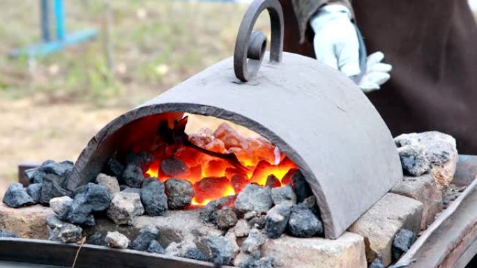 铁匠在热煤中加热钢坯，并准备锻造钢花