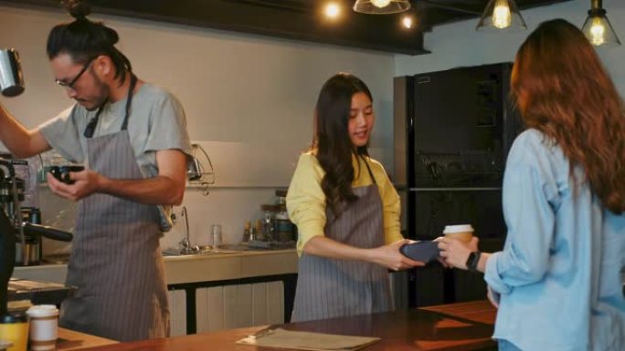 年轻的亚洲女性顾客通过信用卡阅读机进行非接触式支付在咖啡店咖啡厅柜台购买咖啡