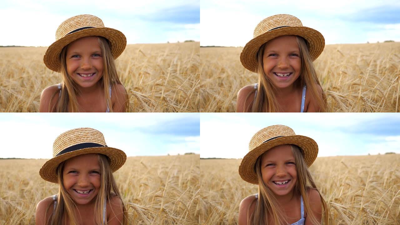小麦草地上金发快乐笑孩子的肖像。戴着草帽的美丽微笑女孩在有机农场大麦田的背景下看着镜头。特写