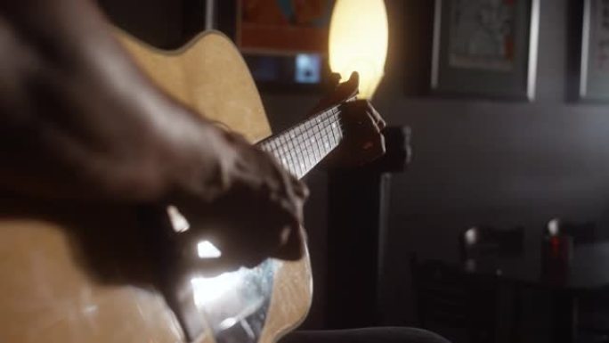 在昏暗的咖啡店里，一位拉丁裔男性音乐家从背后演奏原声吉他的特写镜头