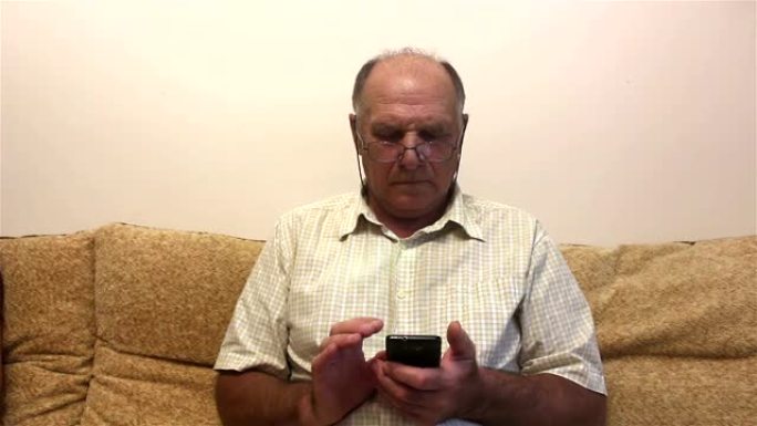 一位老人坐在家里的沙发上，在智能手机上阅读新闻提要。