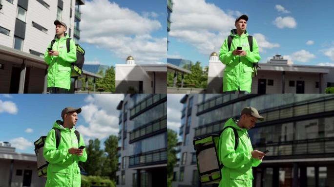 穿着绿色制服的年轻男性食品快递员在智能手机上使用移动导航应用程序在城市街道上用隔热背包平移慢动作镜头