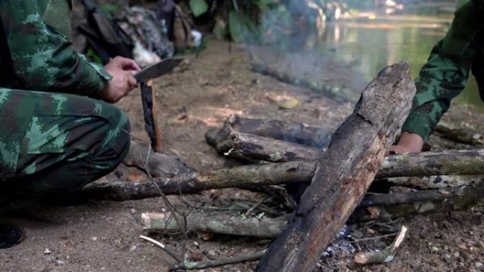 4K Medium拍摄的是两名身穿迷彩服的士兵在小溪附近的露营区用露营刀劈柴生火，准备在森林里做饭。