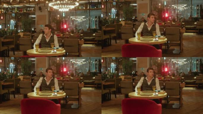英俊的年轻人独自坐在一家时尚的餐厅里环顾四周。男人希望他的女朋友在餐馆里。摄像机从上到下布线。