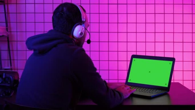 职业玩家在笔记本电脑上玩电子游戏。绿屏模拟显示