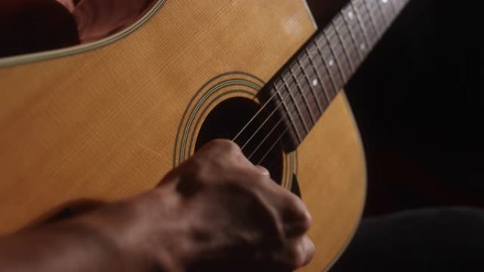 一位拉丁裔男性音乐家的特写镜头，从背后在昏暗的空间里弹奏原声吉他