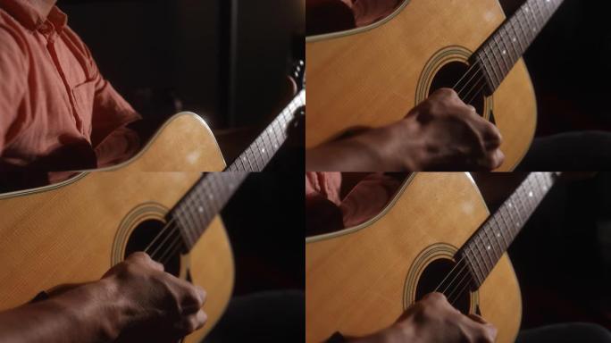 一位拉丁裔男性音乐家的特写镜头，从背后在昏暗的空间里弹奏原声吉他