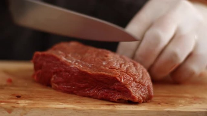 特写4k白手套手工切片红色生牛肉牛排，在木质切片板上，日光，锋利的小刀，黑色围裙，厨师在烹饪前准备肉