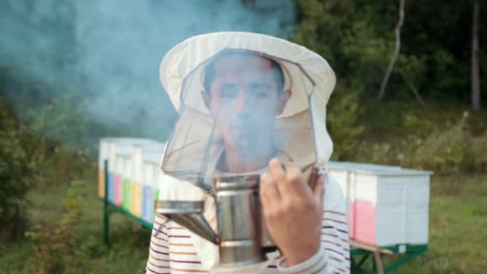 男子养蜂人穿着特殊的衣服，抱着一个吸烟者来平息蜜蜂，大量的烟雾