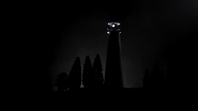 夜晚有雾的光束灯塔。矗立在山上的老灯塔。桌子装饰。色调背景。月光照明。选择性聚焦