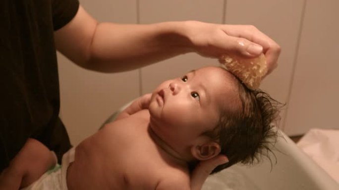洗亚洲婴儿的头发，爸爸的胳膊。在家洗澡，温暖的灯光，白天