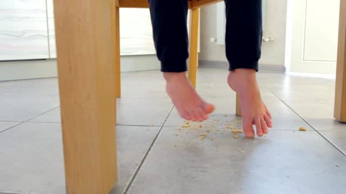 小孩子在餐桌旁吃饭，在地板上碎玉米片。腿和脏地板特写。