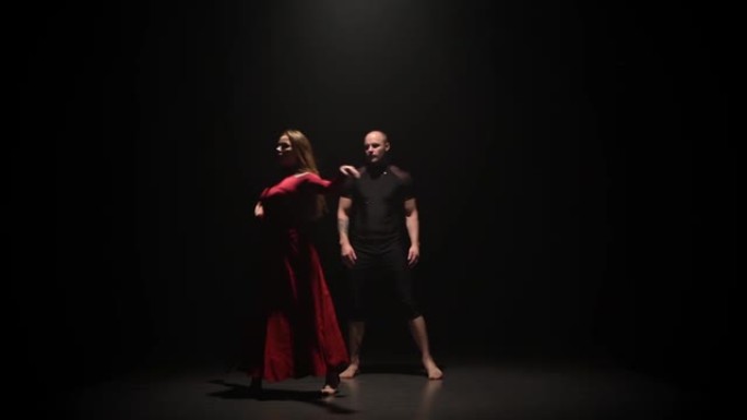 在黑暗的工作室里，女人和男人在聚光灯下的黑色背景上跳舞。慢动作