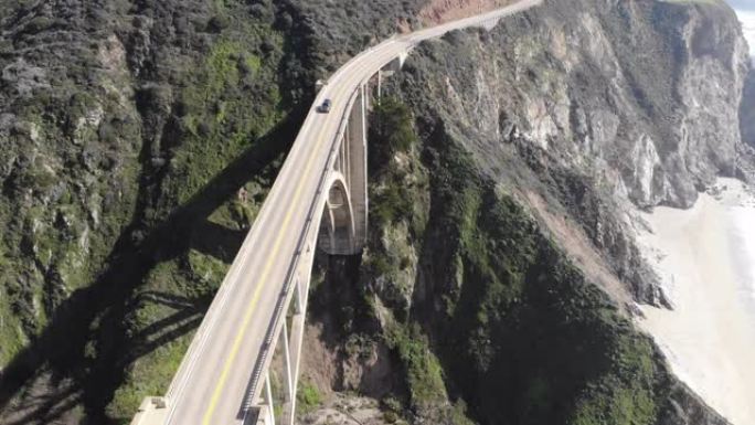Bs42_俯视拱桥，有过往的汽车，缓缓向后移动，抬头露出远处的山脉和道路的跨度，巨大的悬崖俯瞰着海洋