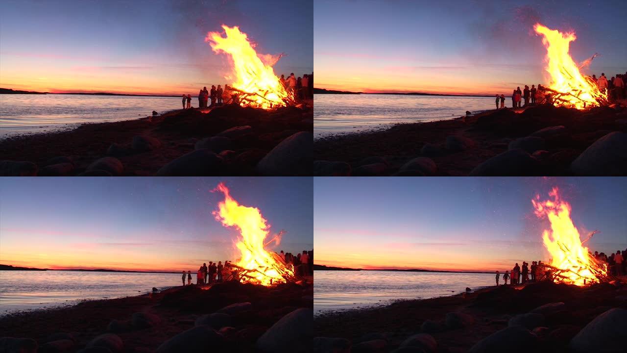 日落时分，在海边的海滩上举行了一场大型篝火晚会。孩子们围着火玩耍。