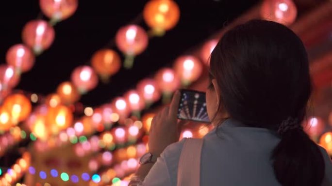 亚洲女人用智能手机拍下上面悬挂的美丽灯笼的照片。