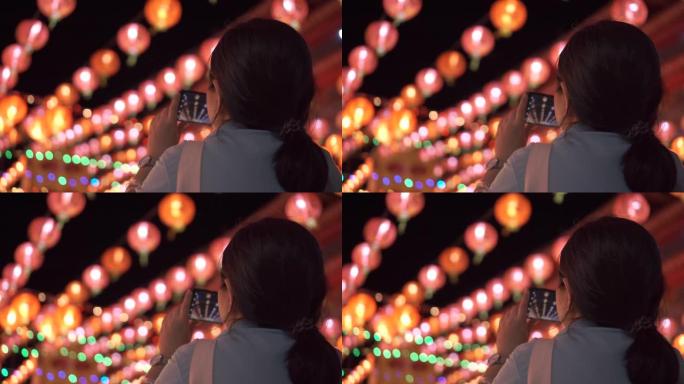 亚洲女人用智能手机拍下上面悬挂的美丽灯笼的照片。