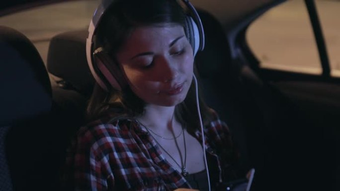 女乘客戴着立体声耳机在汽车上听音乐