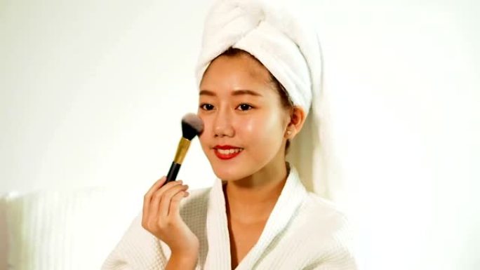 肖像美丽的亚洲女人拿着腮红刷。迷人的年轻女人涂腮红。