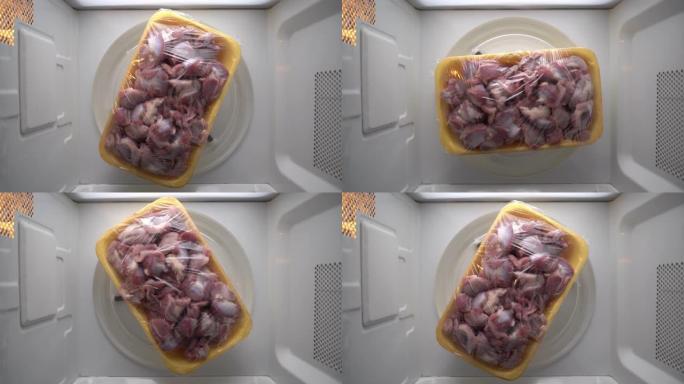 食品托盘中的新鲜生杂碎，保鲜膜在微波炉中旋转。
