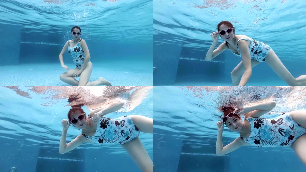 可爱的中年妇女在阳光明媚的日子里以不同的姿势在游泳池水下游泳和摆姿势。她戴着墨镜看着相机，在游泳池底