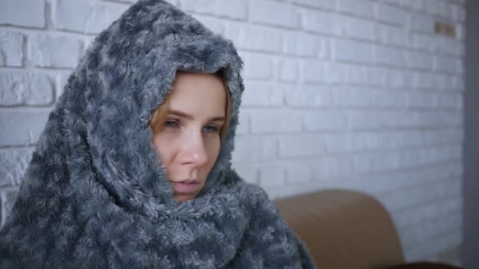 覆盖着灰色格子的年轻白人妇女在家里冻得很冷，生病的女孩有发热流感温度的症状，裹着毯子在室内发抖。特写