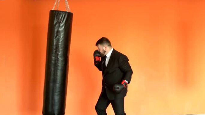 穿着黑色西装的愤怒商人减轻了健身俱乐部的压力。穿着拳击手套的经理或老板在斯洛莫的健身房击败沙袋。留着