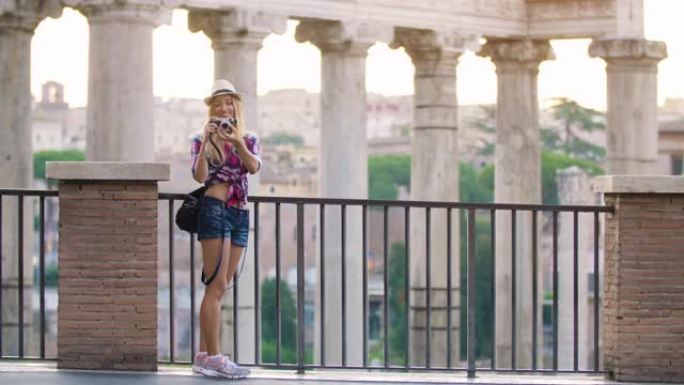 日出时，长发和蓝眼睛的快乐年轻金发女子在罗马论坛用老式相机拍照。意大利罗马。镜头上的眼睛。