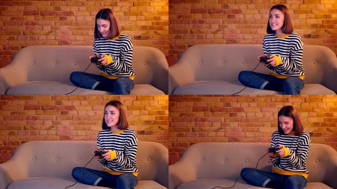 在室内舒适的公寓里，使用游戏机玩电子游戏的年轻漂亮女孩的特写肖像兴奋地坐在沙发上