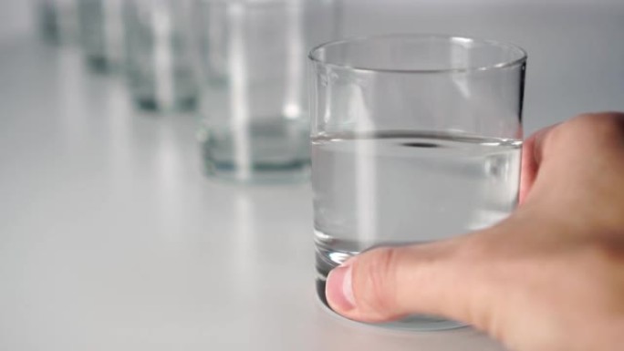 一只手在酒吧的灰色桌子上的一排眼镜中挥动透明液体