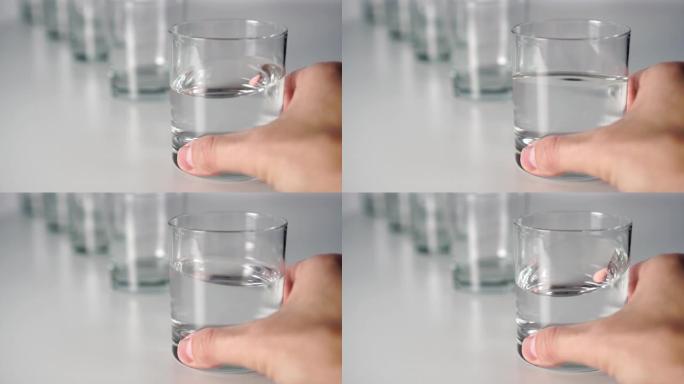一只手在酒吧的灰色桌子上的一排眼镜中挥动透明液体