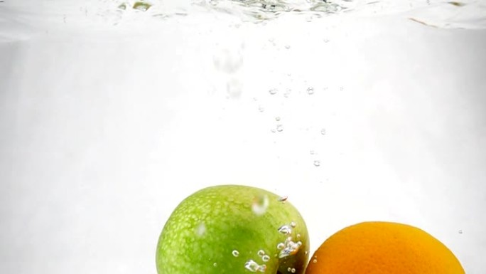 橙色和青苹果在水中以慢动作旋转的气泡旋转。