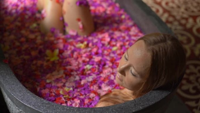 一个美丽的年轻女子在热带水疗中心洗花浴的慢镜头