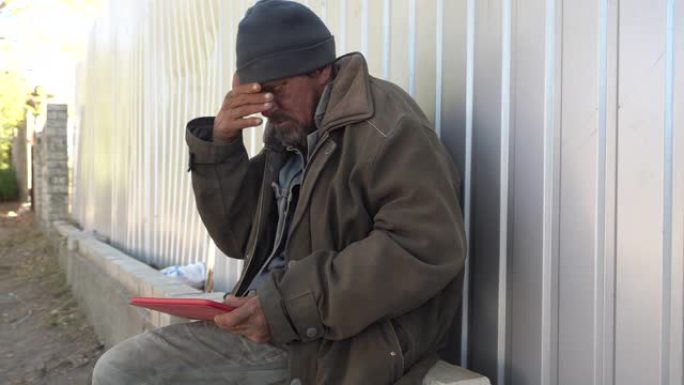 无家可归的人在户外使用数字平板电脑。乞丐坐在街上