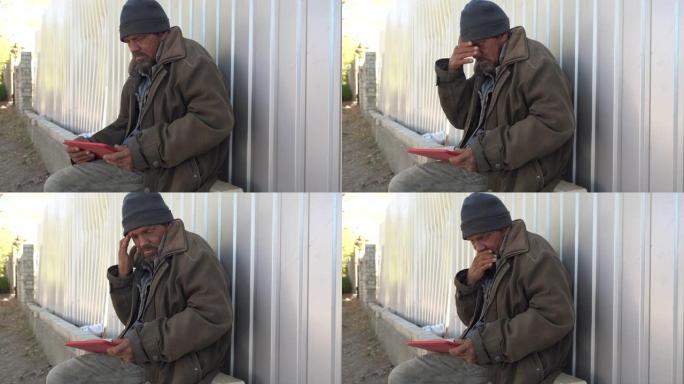 无家可归的人在户外使用数字平板电脑。乞丐坐在街上