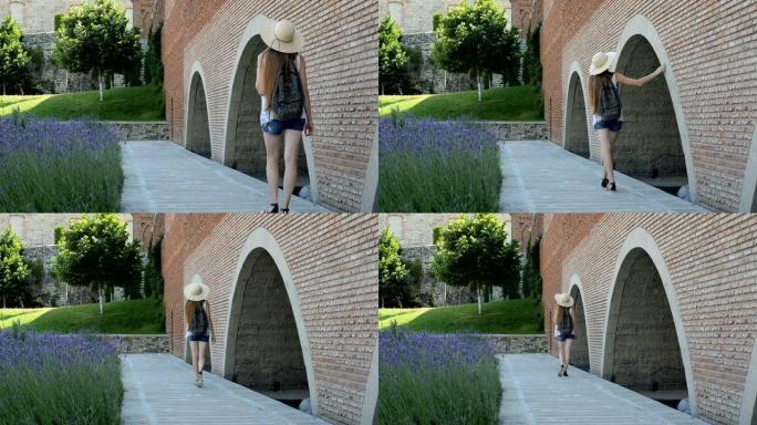 戴着帽子的年轻女子沿着古老的墙壁行走并抚摸她