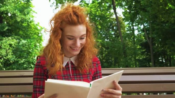 快活的红发女孩在公园里嘲笑有趣的书