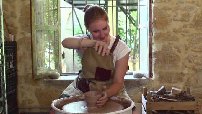 女人在陶工的轮子上工作，擦额头。双手用陶罐雕刻杯子。