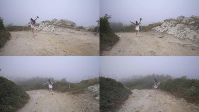 穿着白色连衣裙、格子t恤和staw帽子的跑步旅行者女孩在雾中沿着乡间小路奔跑。风。葡萄牙辛特拉。