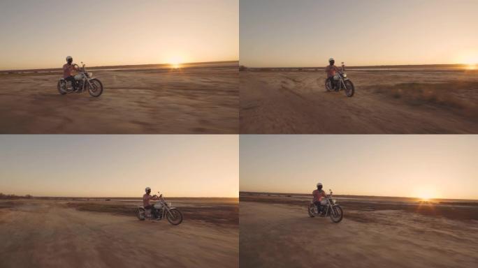 年轻时尚的摩托车手在日落时在沙漠路上驾驶摩托车