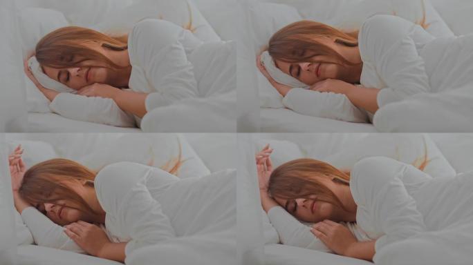 美丽的女孩睡在白色毯子下的床上。舒适的房间，床上有白色枕头。肖像视图。