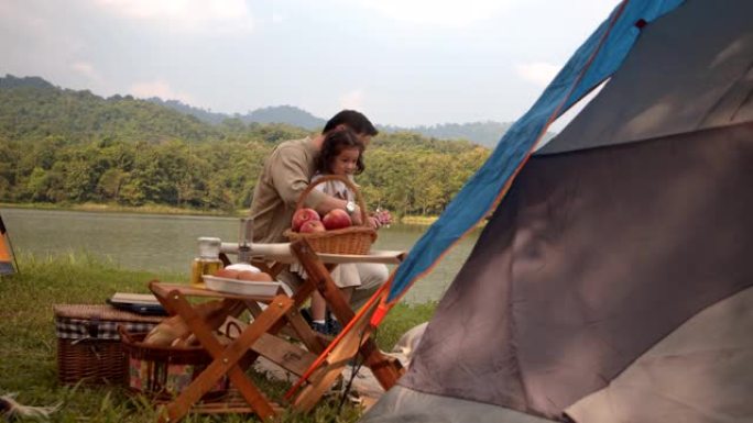 亚洲家庭父亲母亲和女儿在阳光明媚的夏天在公园的自然森林露营时坐着聊天玩耍。周末的家庭活动。4k镜头。